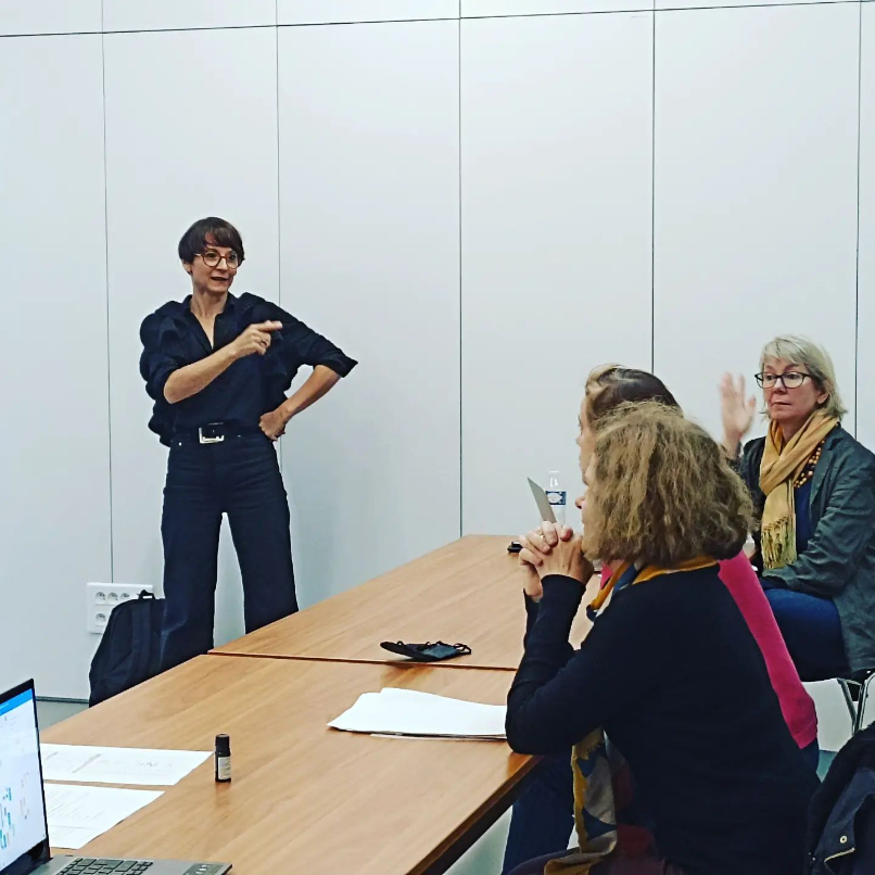 Photo en salle de réunion avec Émilie BOUGOUIN expliquant les points essentiels de la formation, debout, face aux participantes.