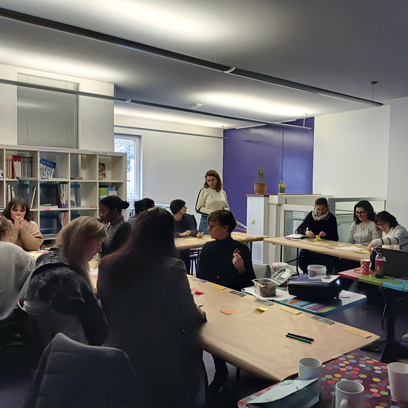 Nouvelle séance de formation, 11 participants et émilie Bougouin assis aux tables en pleine réflexion, échange de post it.