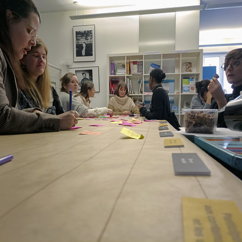 Gros plan sur la table et les post it d'un groupe de 7 participantes et émilie Bougouin. à côté une grosse boîte de biscuit aux chocolats !
